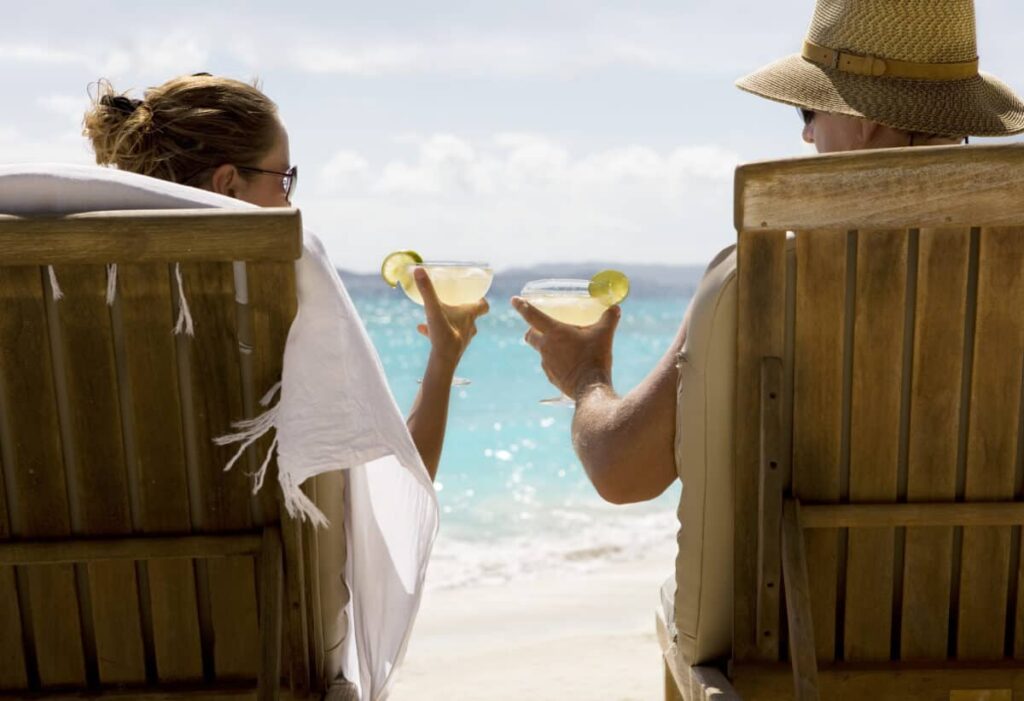 2 Canadian Dividend Stocks I’d Buy and Hold for Life people sit in two wooden beach chairs facing the Caribbean ocean holding drinks and making a toast
